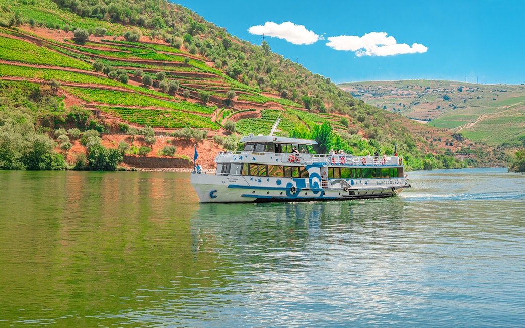 Cruise boat on Douro River with terraced vineyards in Douro Valley, Portugal.