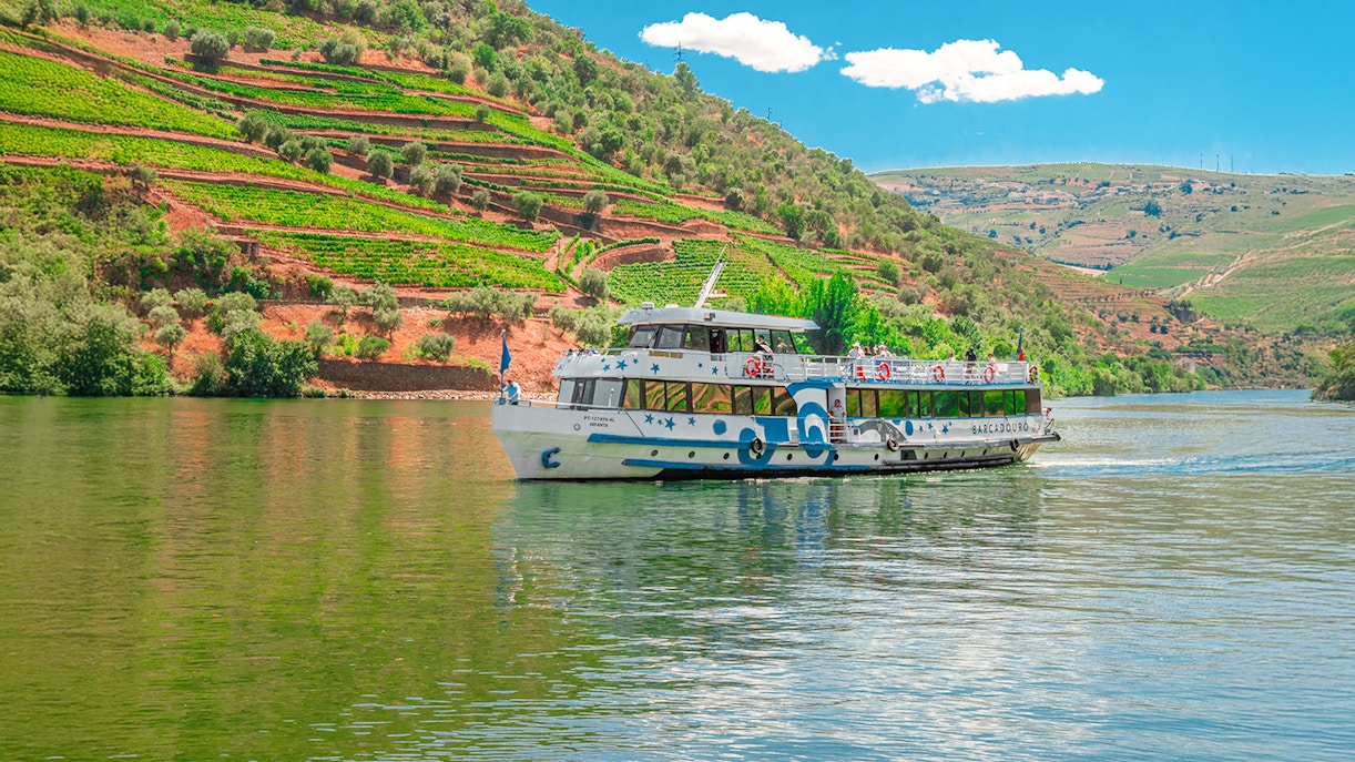 Cruise boat on Douro River with terraced vineyards in Douro Valley, Portugal.