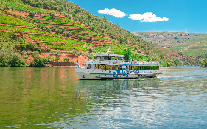 Cruise boat on Douro River with terraced vineyards in Douro Valley, Portugal.