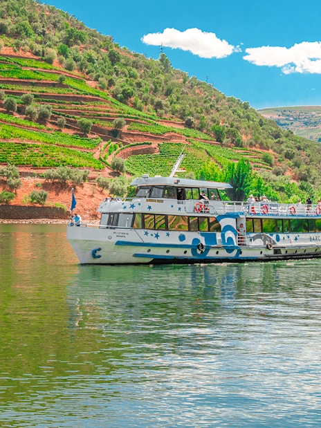 Cruise boat on Douro River with terraced vineyards in Douro Valley, Portugal.