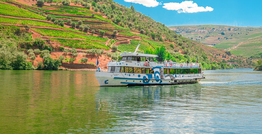 Cruise boat on Douro River with terraced vineyards in Douro Valley, Portugal.
