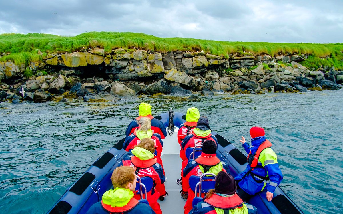 Guests on a boat tour approaching Puffin Island's rocky shoreline.