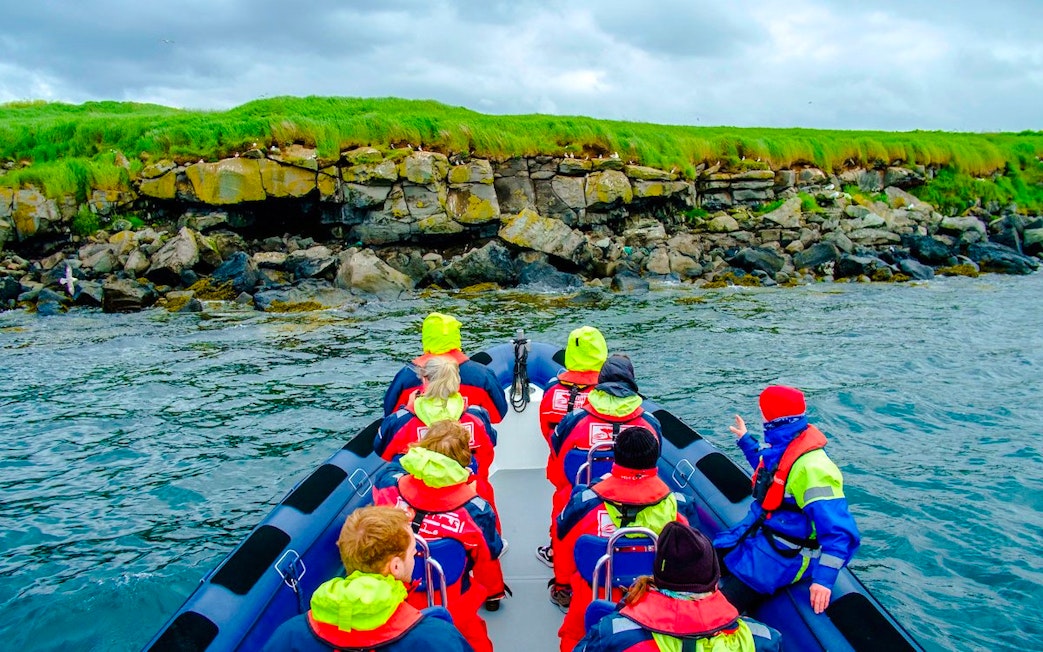 Guests on a boat tour approaching Puffin Island's rocky shoreline.