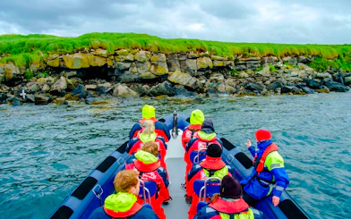 Guests on a boat tour approaching Puffin Island's rocky shoreline.