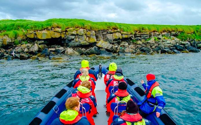 Guests on a boat tour approaching Puffin Island's rocky shoreline.