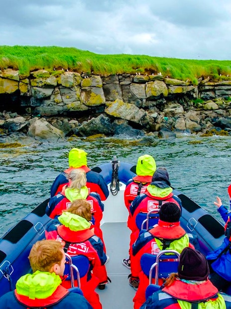 Guests on a boat tour approaching Puffin Island's rocky shoreline.