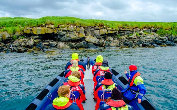 Guests on a boat tour approaching Puffin Island's rocky shoreline.