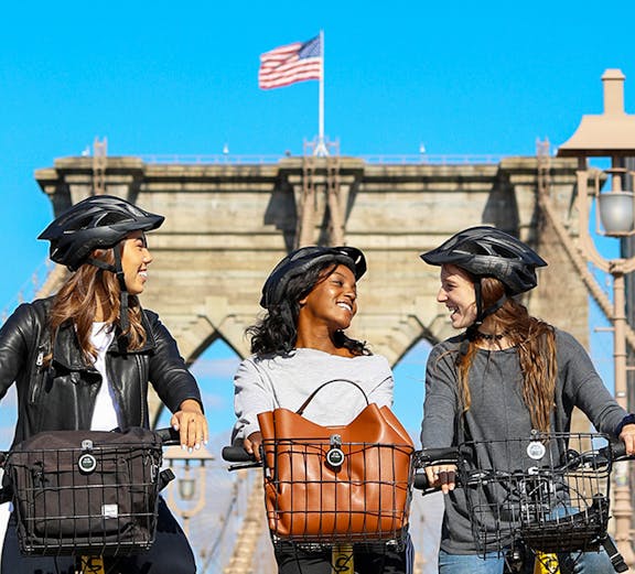 Three people biking on the Brooklyn Bridge, New York City, with rental bikes.