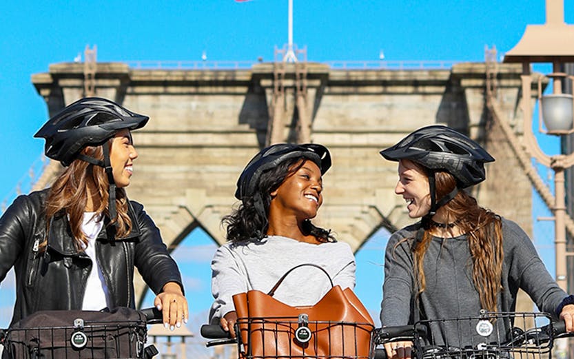 Three people biking on the Brooklyn Bridge, New York City, with rental bikes.