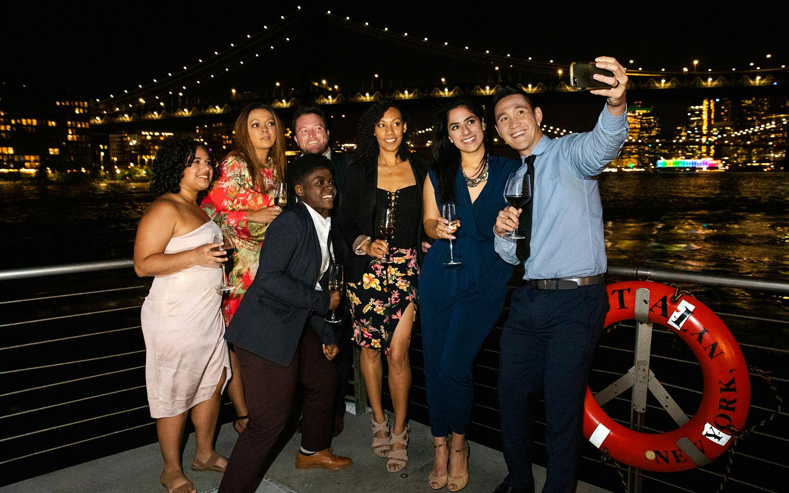 Group enjoying a night cruise with city skyline and bridge in the background, New Jersey Signature Cruise.