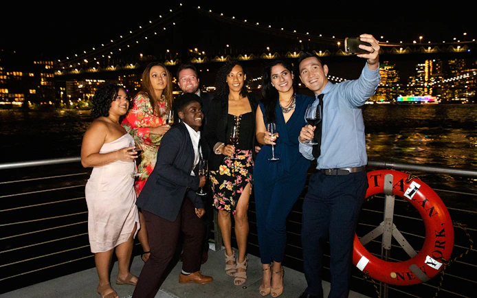Group enjoying a night cruise with city skyline and bridge in the background, New Jersey Signature Cruise.