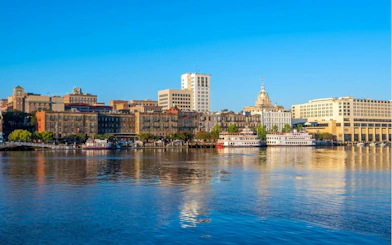 Savannah riverfront with historic buildings and riverboats, part of the self-guided city exploration game.