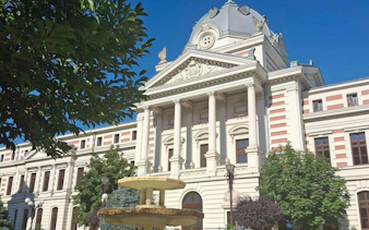 Historic building with columns and fountain, part of The Vanishing Pharmacist game, Bucharest.