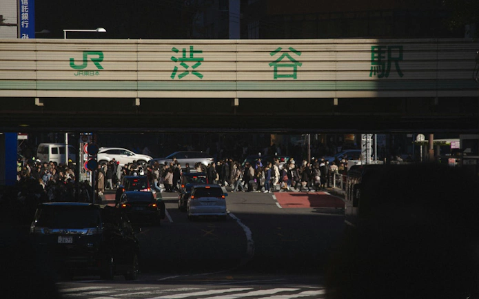 Crowds crossing Shibuya Crossing under JR sign in Tokyo during guided walking tour.