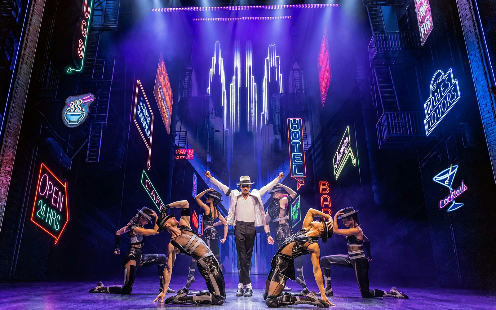 Performer in white hat and dancers on stage with neon city backdrop in MJ The Musical.