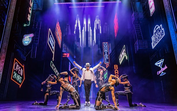Performer in white hat and dancers on stage with neon city backdrop in MJ The Musical.