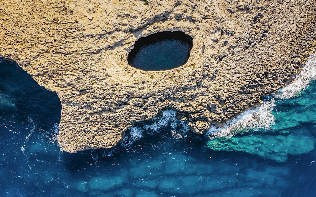 Aerial view of Ahrax fallen cave and Coral Lagoon, Malta with surrounding sea.