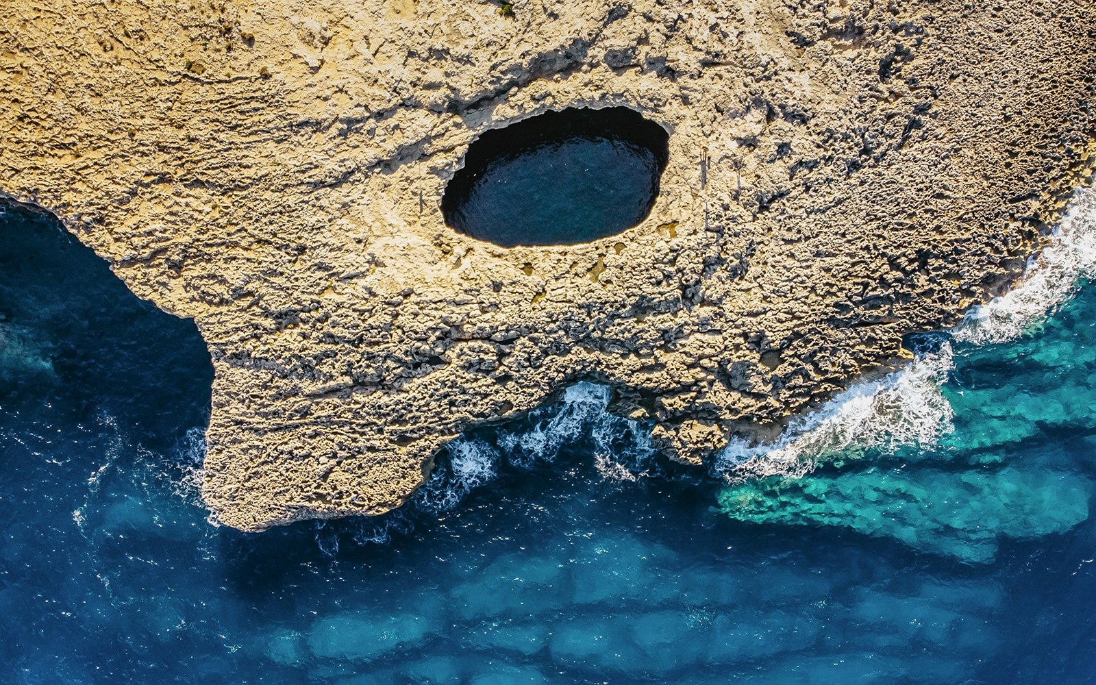 Aerial view of Ahrax fallen cave and Coral Lagoon in Malta showcasing natural rock formations and turquoise waters.