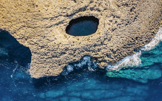 Aerial view of Ahrax fallen cave and Coral Lagoon, Malta with surrounding sea.