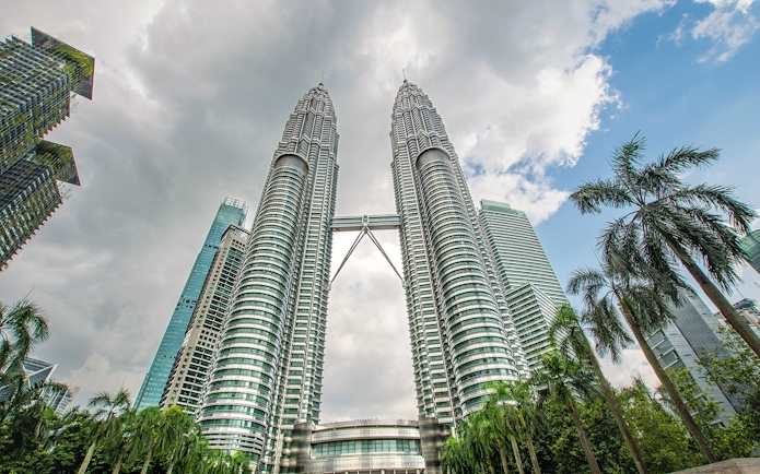 Petronas Twin Towers in Kuala Lumpur with surrounding skyscrapers and palm trees.