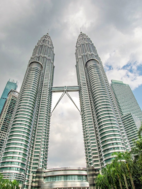 Petronas Twin Towers in Kuala Lumpur with surrounding skyscrapers and palm trees.