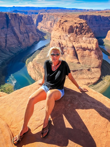 Horseshoe Bend view with person sitting on rock, part of Secret Antelope Canyon tour.
