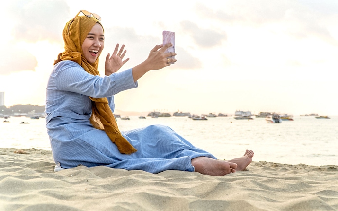 Woman on beach video calling with smartphone, Kuala Lumpur 5G SIM Card.