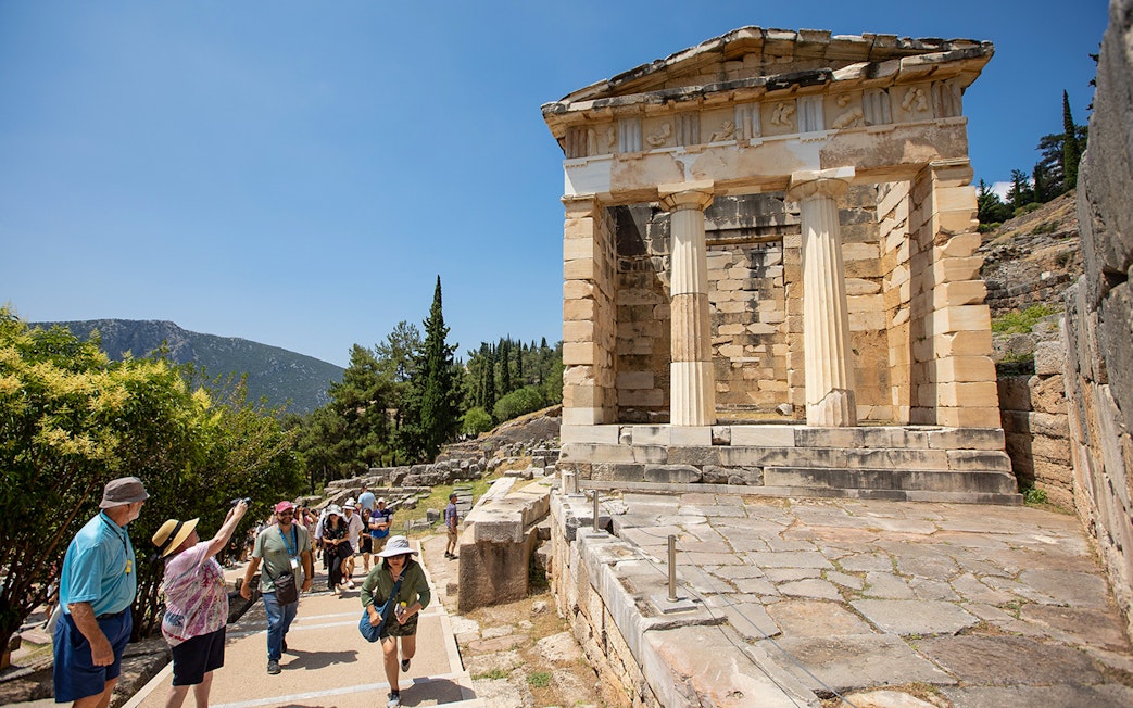 Visitors walking near the ancient ruins of the Treasury of Athens at Delphi, Greece.