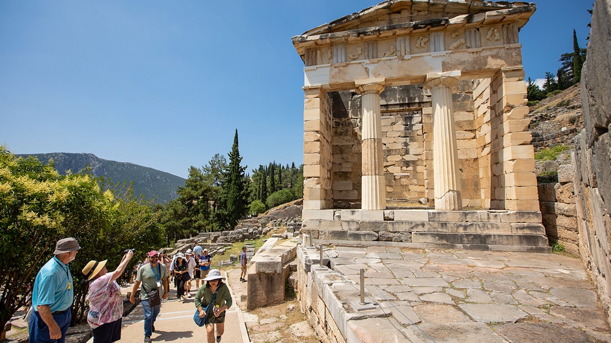 Visitors walking near the ancient ruins of the Treasury of Athens at Delphi, Greece.