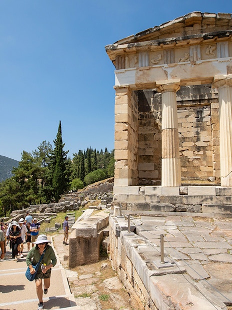 Visitors walking near the ancient ruins of the Treasury of Athens at Delphi, Greece.