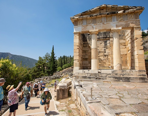 Visitors walking near the ancient ruins of the Treasury of Athens at Delphi, Greece.