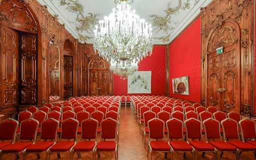 Vienna Baroque concert hall with ornate woodwork and red seating.