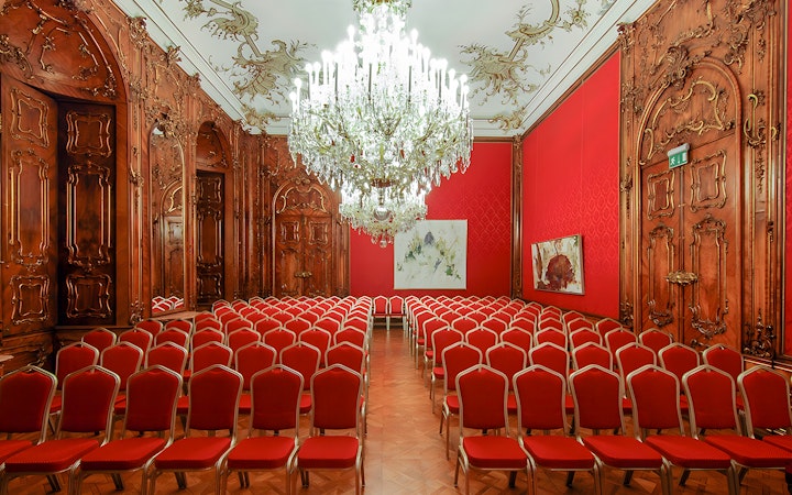 Vienna Baroque concert hall with ornate woodwork and red seating.