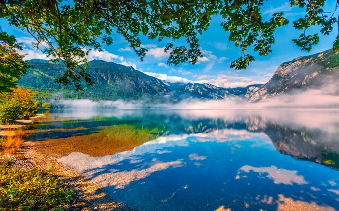 Bohinj Lake with misty mountains and clear reflections in Slovenia.