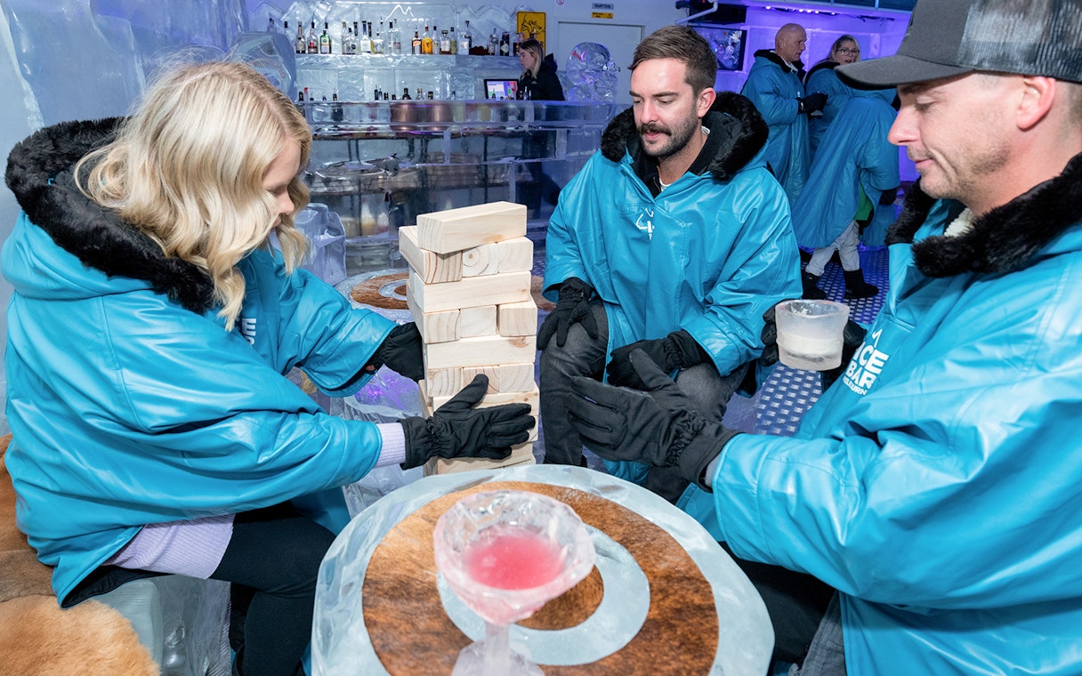 Guests playing Jenga at IceBar Surfers Paradise, wearing blue parkas and holding drinks.