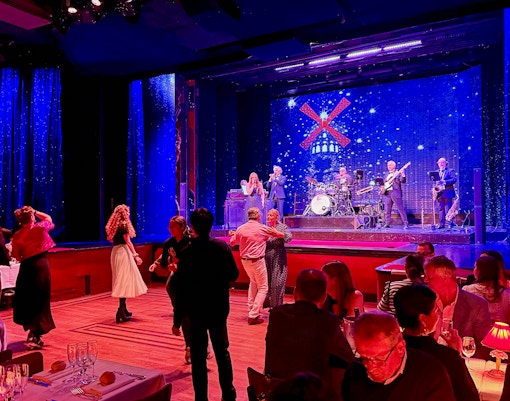 Guests dancing at Moulin Rouge pre-show in Paris with live band on stage.