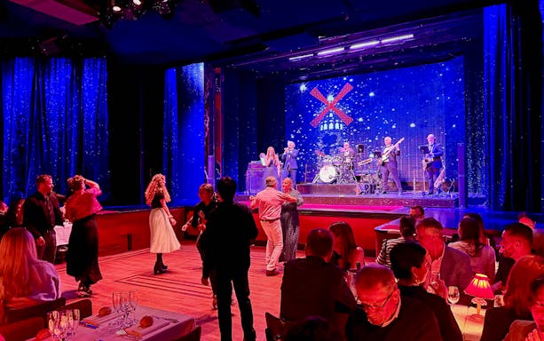 Guests dancing at Moulin Rouge pre-show in Paris with live band on stage.