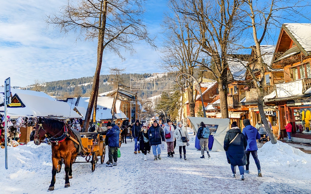 Pedestrians walking on snowy Krupówki Street in Zakopane with horse-drawn carriage.