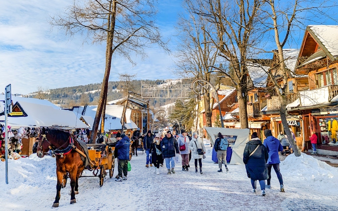 Pedestrians walking on snowy Krupówki Street in Zakopane with horse-drawn carriage.
