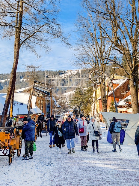 Pedestrians walking on snowy Krupówki Street in Zakopane with horse-drawn carriage.