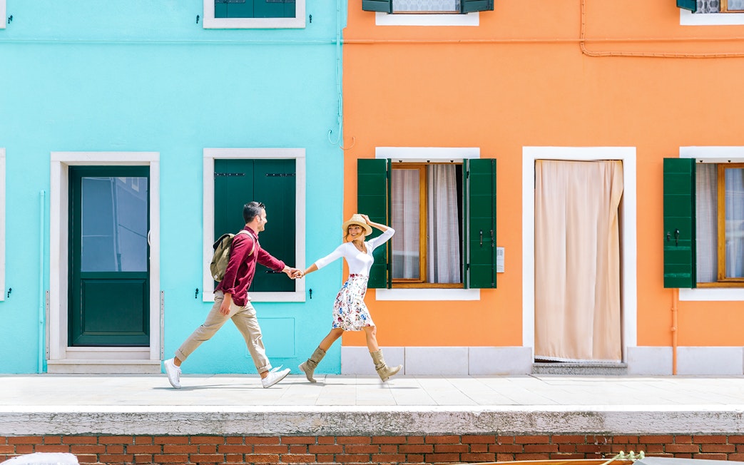 Couple walking past colorful houses in Burano, Italy.