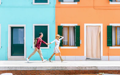 Couple walking past colorful houses in Burano, Italy.