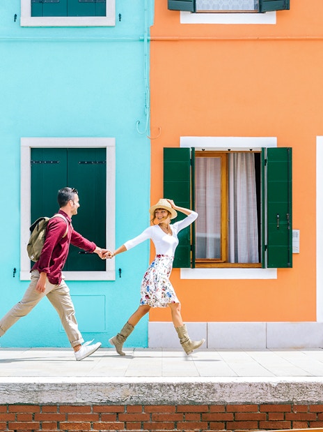 Couple walking past colorful houses in Burano, Italy.