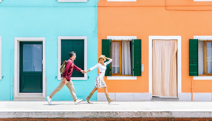 Couple exploring colorful houses along a canal in Burano, Italy.