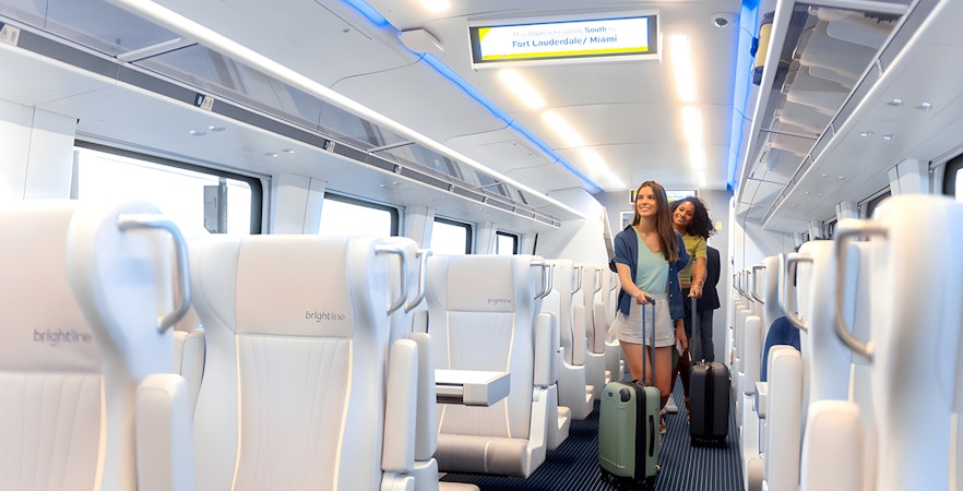 Two women with luggage walking inside a Brightline train to Fort Lauderdale/Miami.