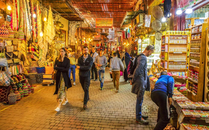 Marrakech market with people browsing colorful textiles and spices.