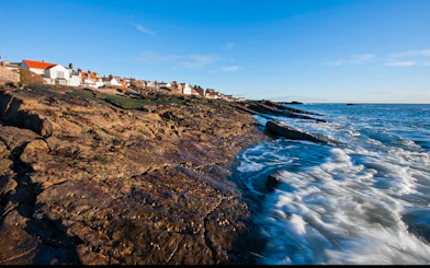 Coastal view of fishing village in Fife, Scotland, with rocky shoreline and ocean waves.
