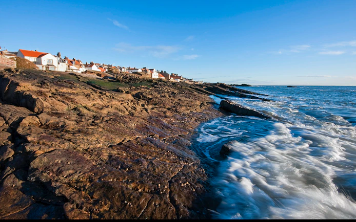 Coastal view of fishing village in Fife, Scotland, with rocky shoreline and ocean waves.