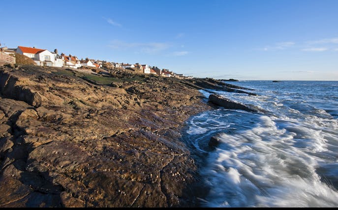 Coastal view of fishing village in Fife, Scotland, with rocky shoreline and ocean waves.