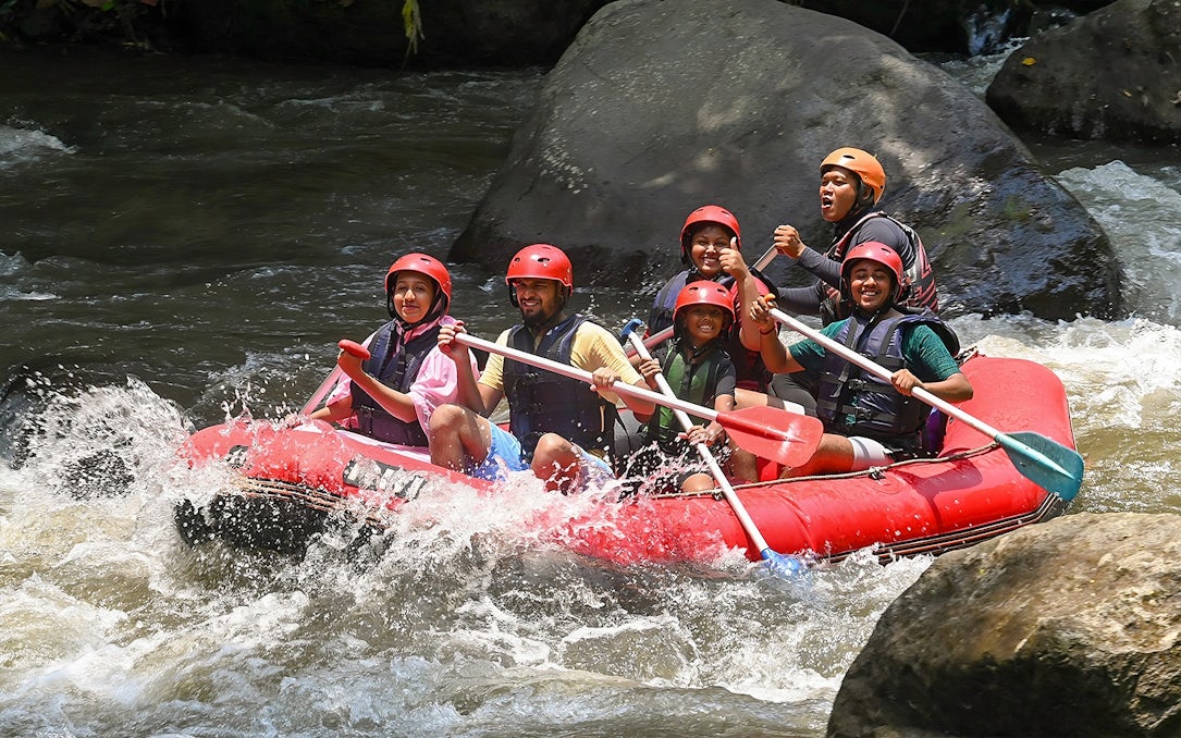 Group rafting on Ayung River in Ubud, navigating rapids in a red inflatable raft.